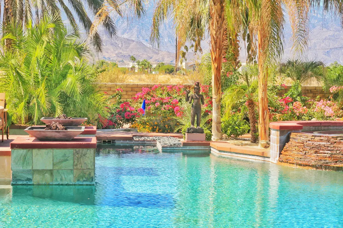 Backyard pool with fire bowls, a stacked-stone spillover spa and palm trees, with desert mountains behind