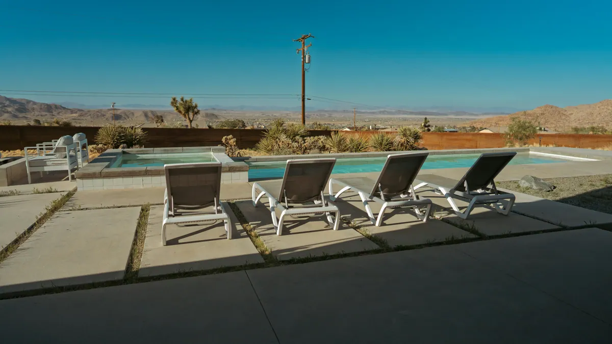Pool and raised spa with four lounge chairs on a concrete deck, Joshua trees and desert hills beyond