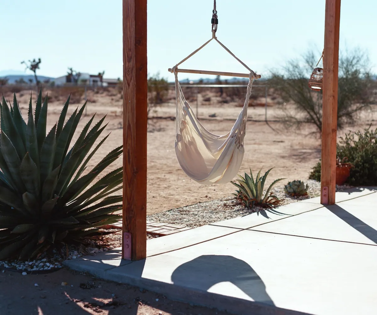 Concrete patio with wood posts, a hanging hammock chair, agave and gravel landscaping facing open desert