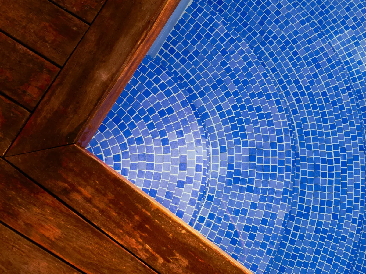 Blue mosaic tile on curved pool steps beside a wood deck edge