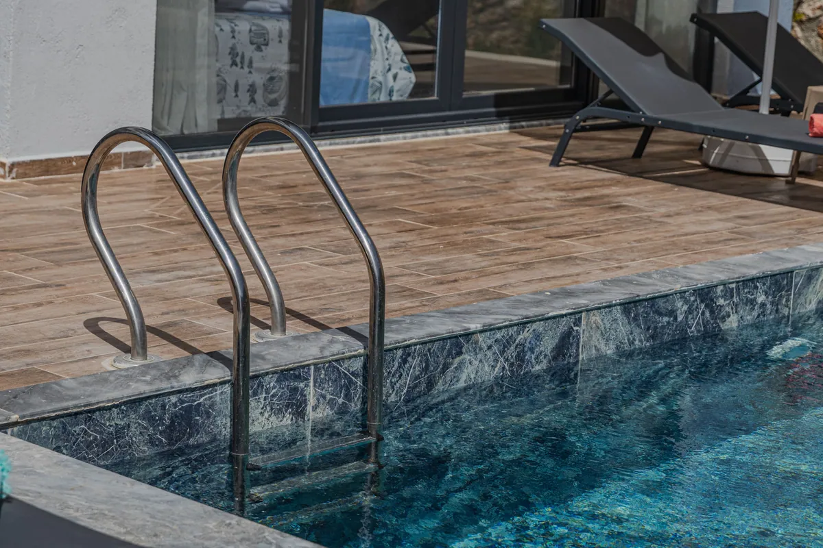 Pool ladder beside dark marble-look waterline tile and a tiled deck