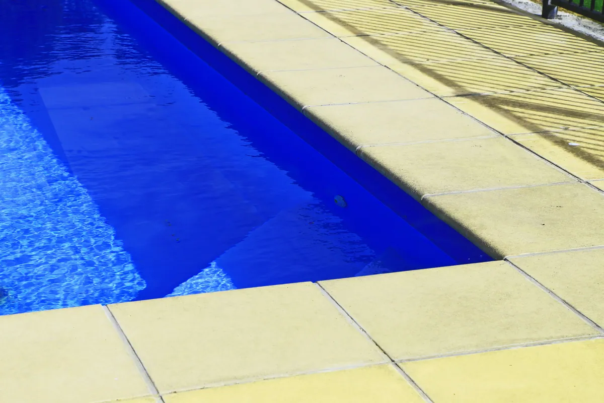 Corner of a pool with light paver coping and bright blue water