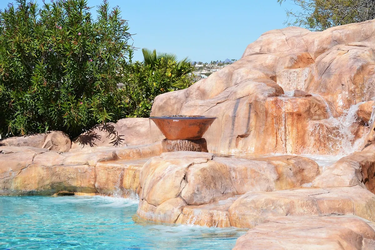 Pool with a sculpted rock waterfall and a copper fire bowl beside flowering shrubs
