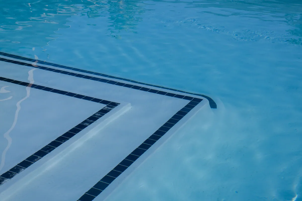 Clear blue water over a smooth light pool interior, with dark tile lines marking the step edges