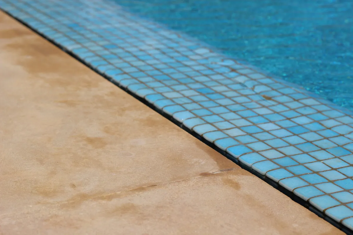 Blue mosaic waterline tile where the pool meets a concrete deck