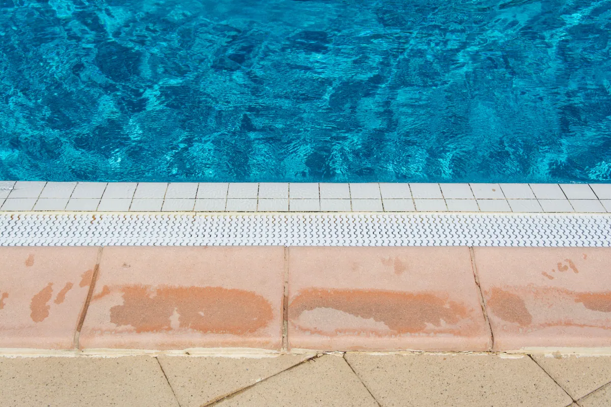 Pool edge with white waterline tile, a gutter grate and weathered stone coping