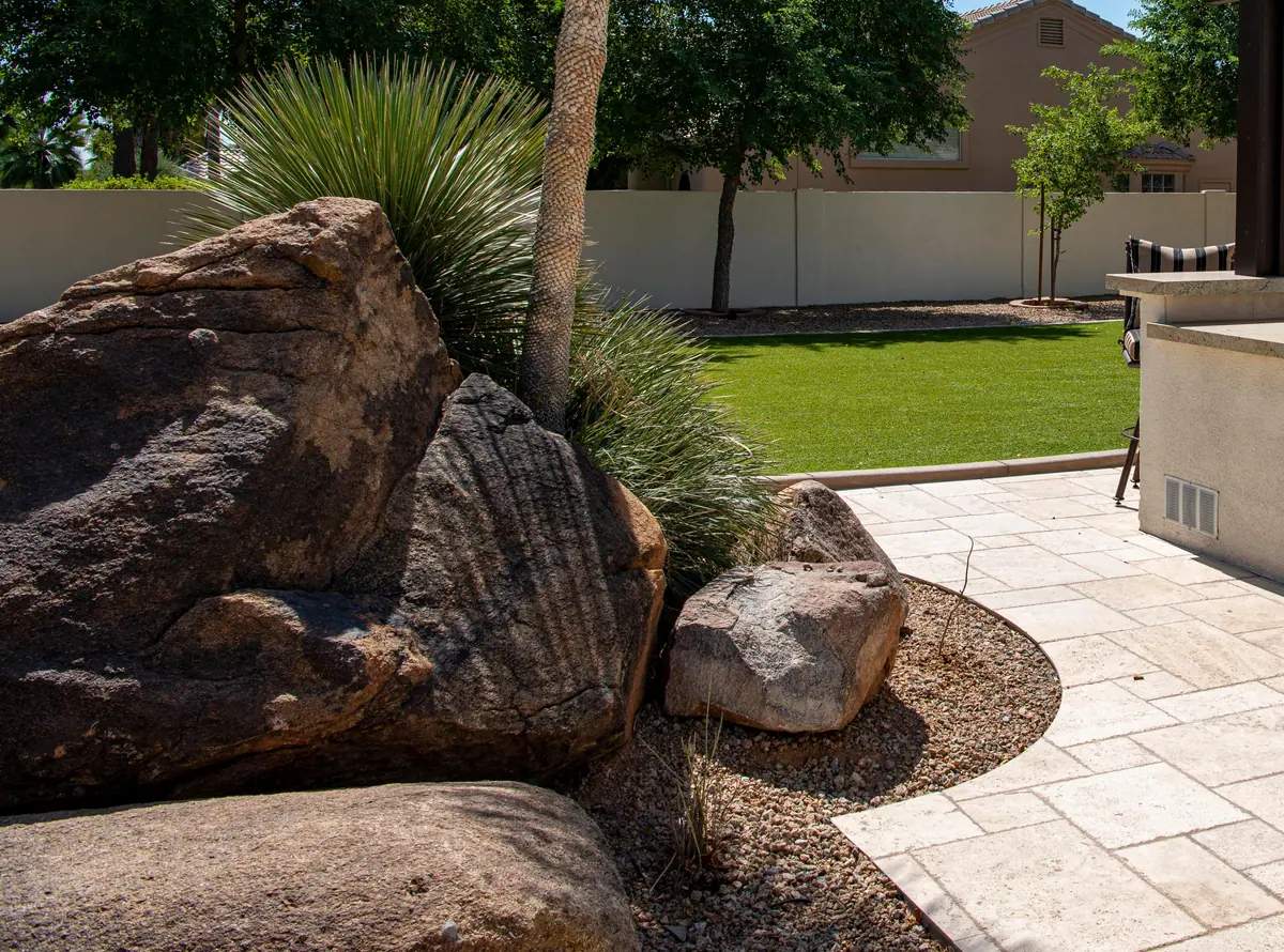 Travertine paver patio curving around large boulders and desert plants, with a block wall behind